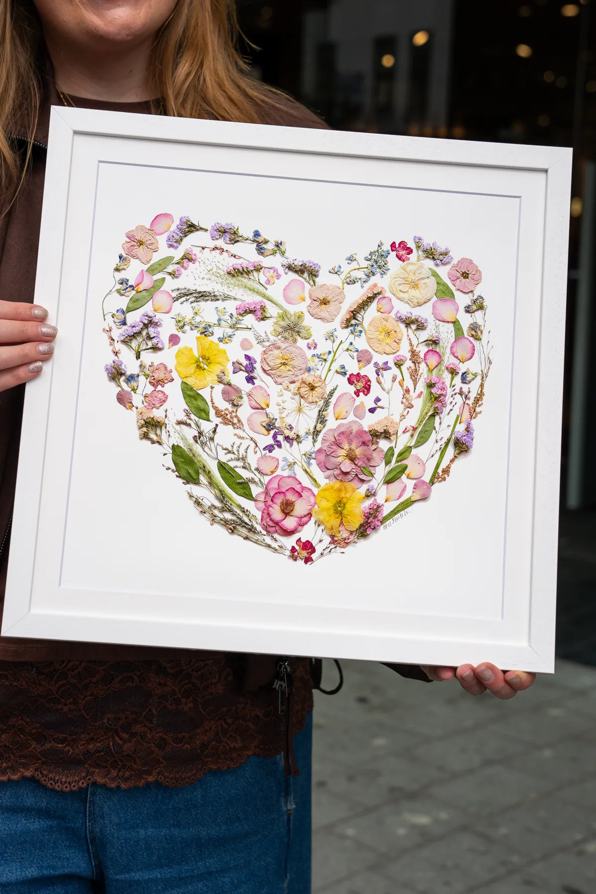 A pressed flower heart in a white frame