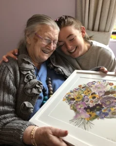 Nell and her Nana Nancy laughing over a framed pressed bouquet