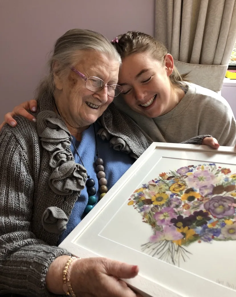Nell and her Nana Nancy laughing over a framed pressed bouquet