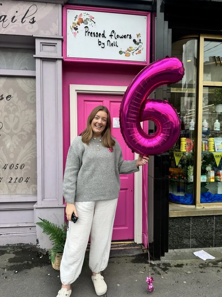 Nell at the pink studio door with a big number six balloon