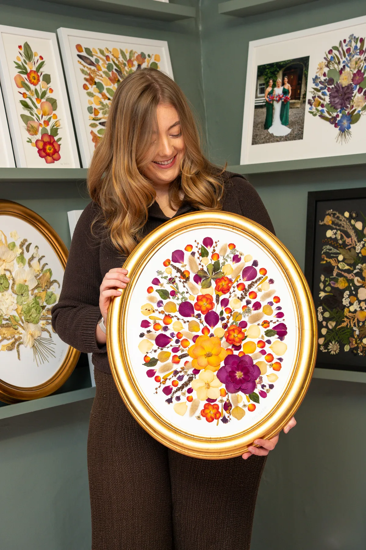 Nell holding a gold oval frame of pressed bridal flowers in the studio