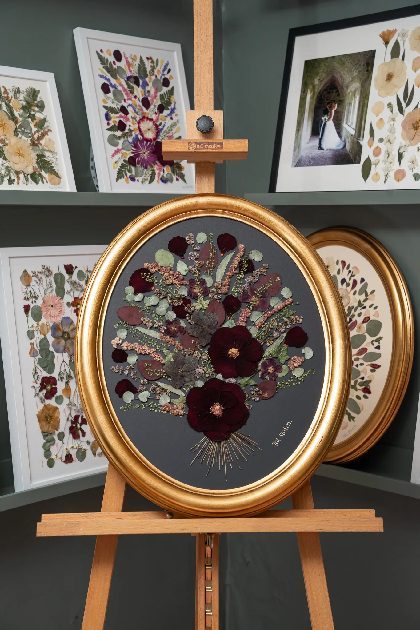 A finished pressed bouquet in a gold oval frame on the studio easel