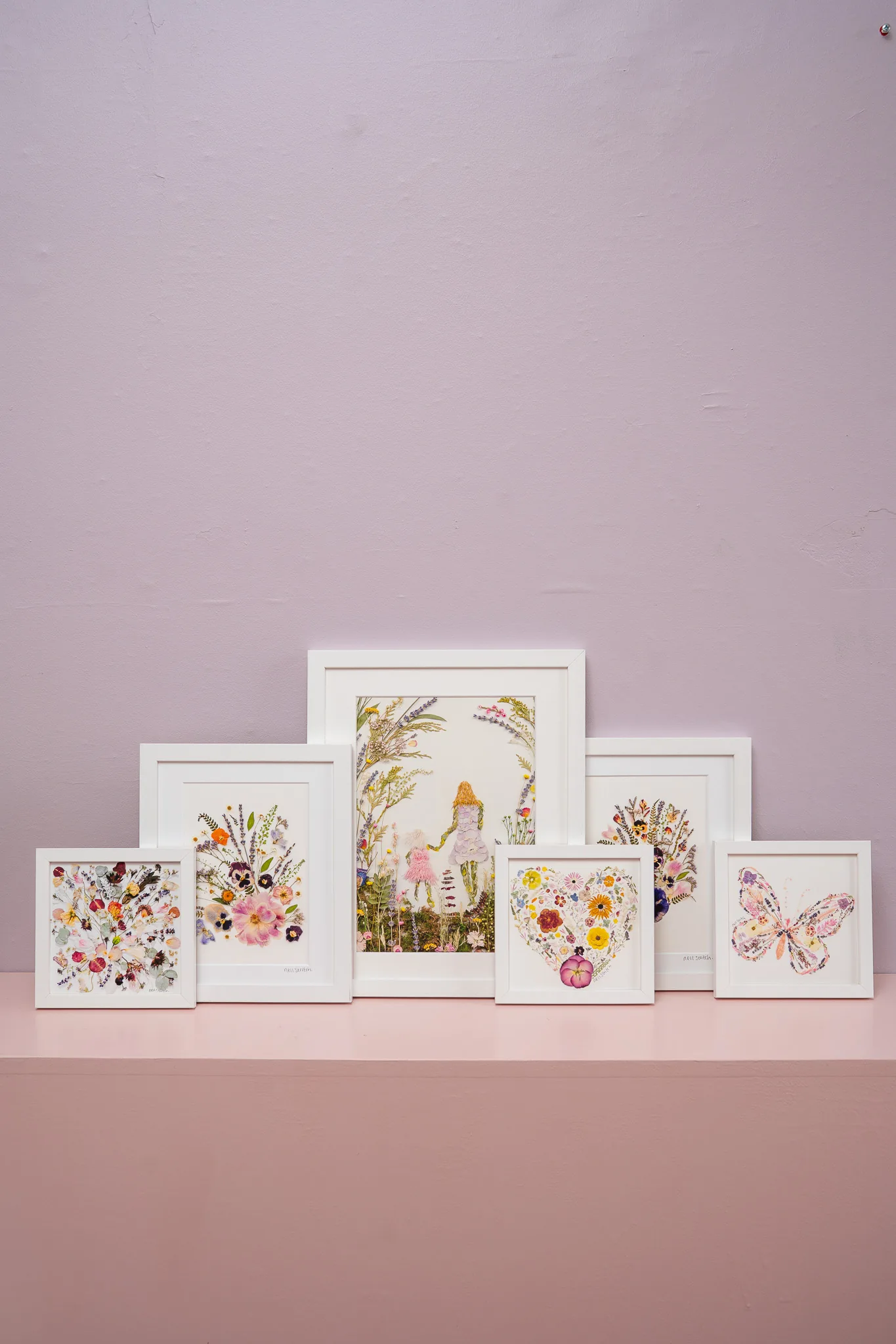 Framed pressed flower prints in a row on the pink shelf
