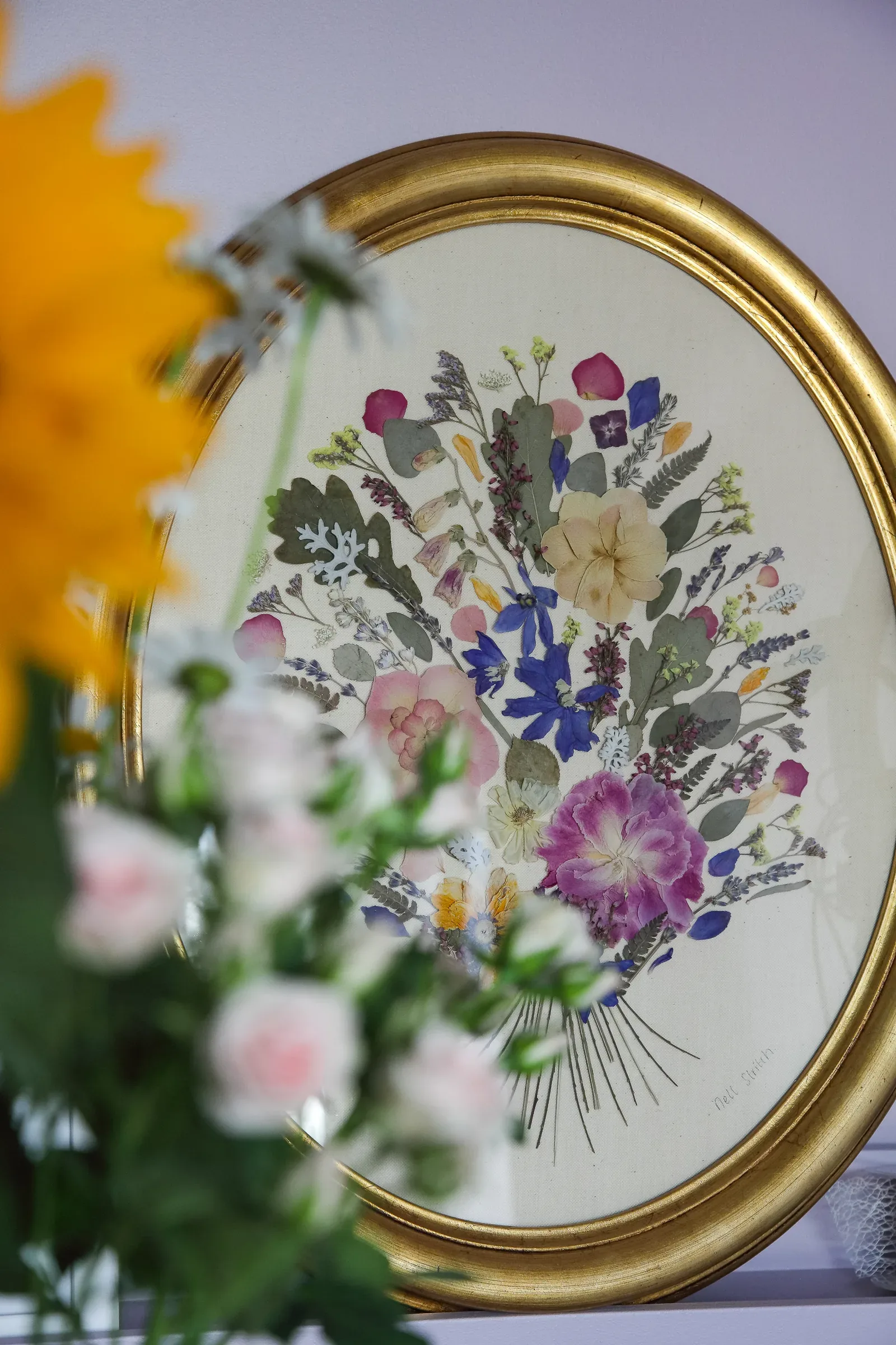 A gold oval frame of pressed flowers beside fresh blooms