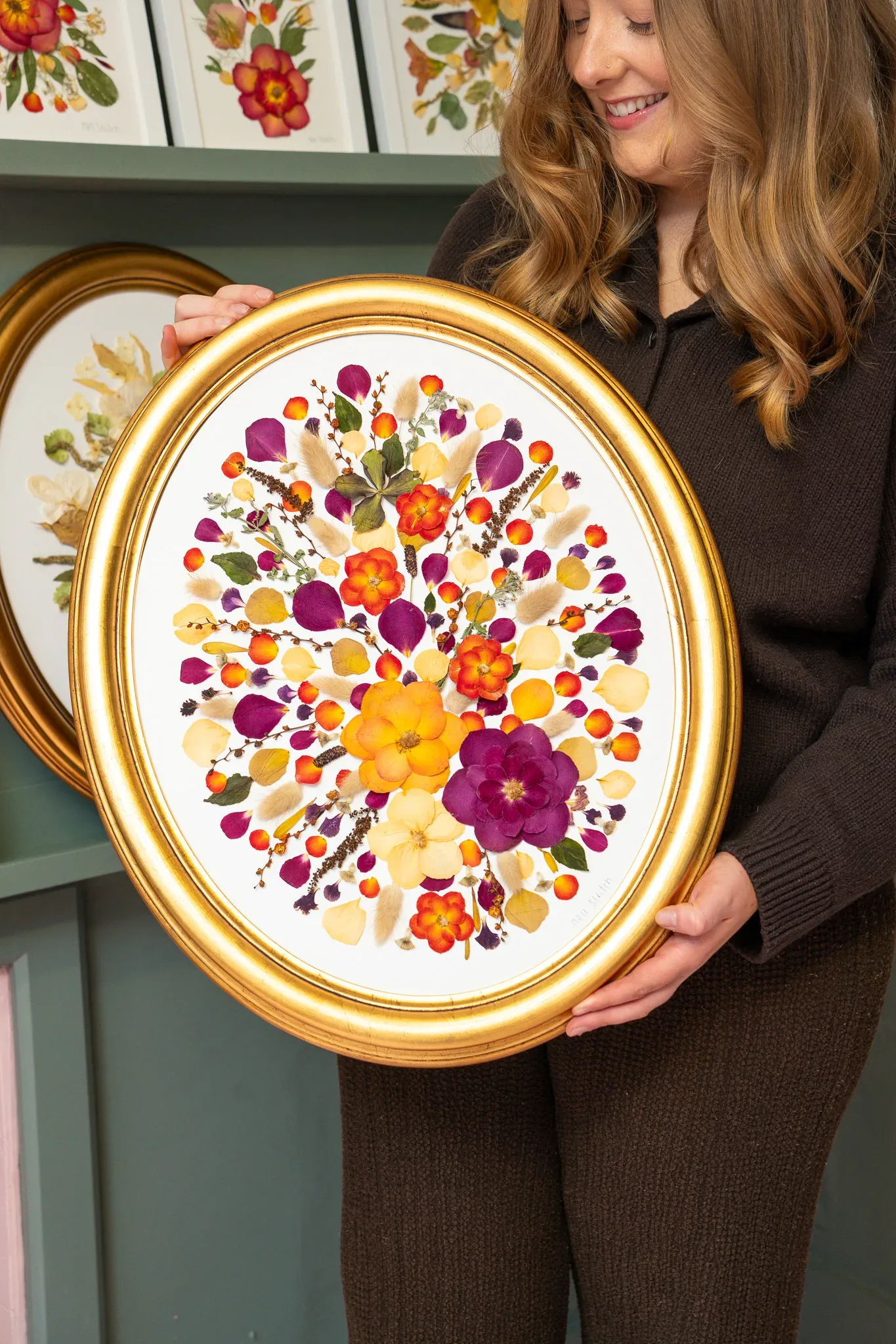 Nell holding a gold oval frame of pressed flowers