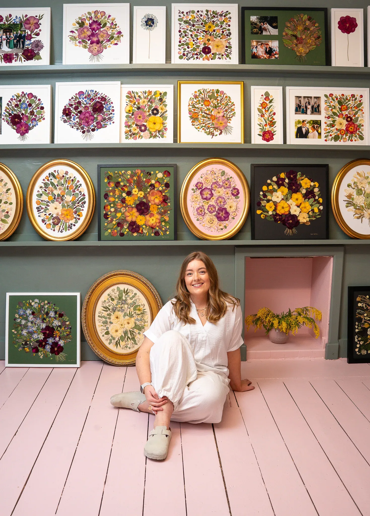 Nell sitting on the pink studio floor among framed pressed flowers