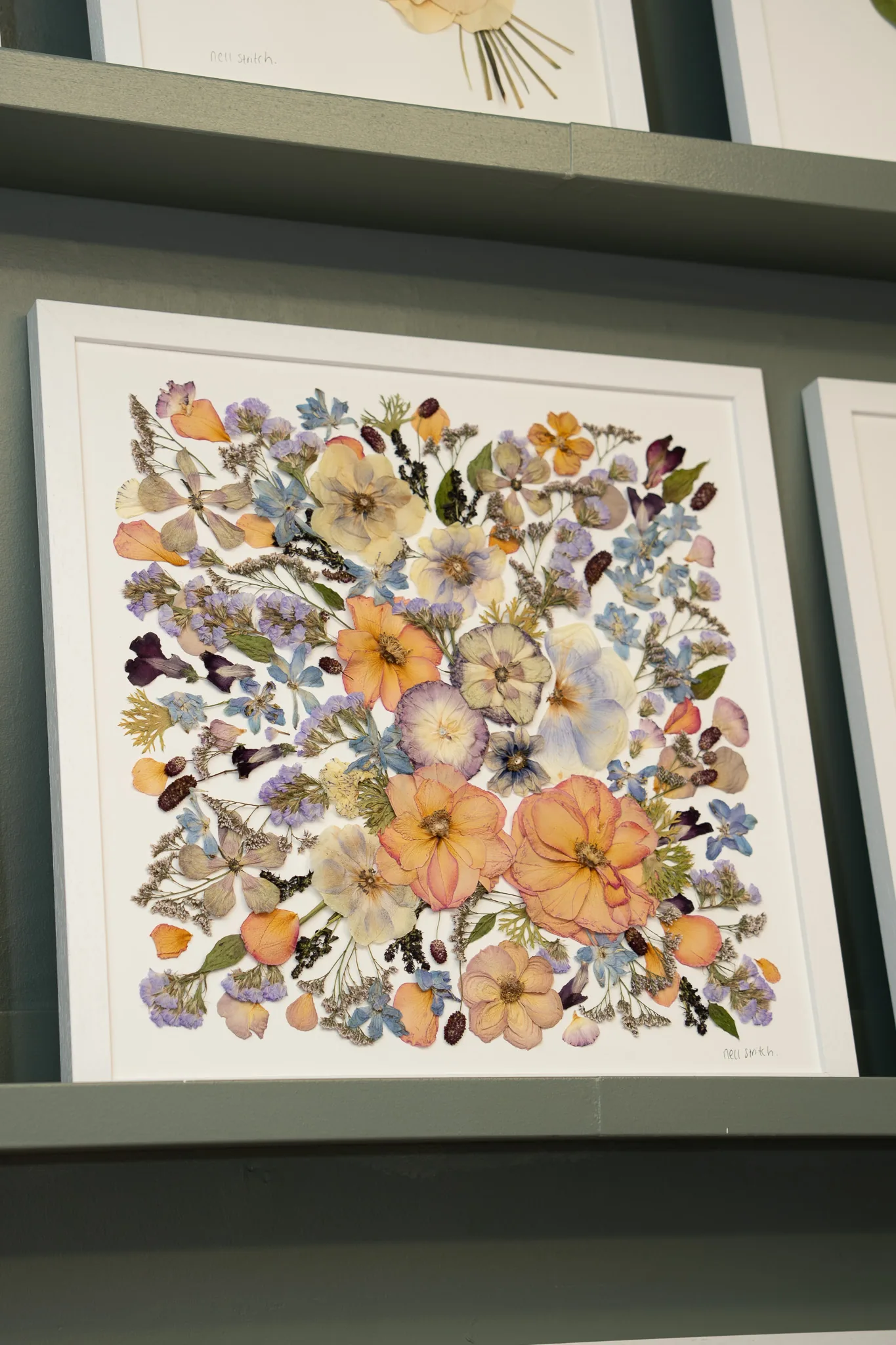 A large square pressed flower bouquet in a white frame