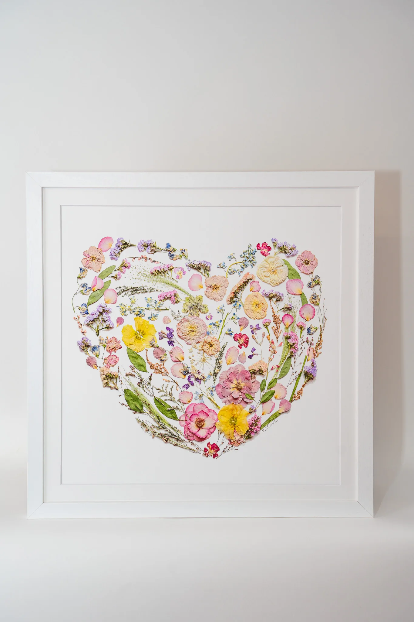 A pressed flower heart in a white frame