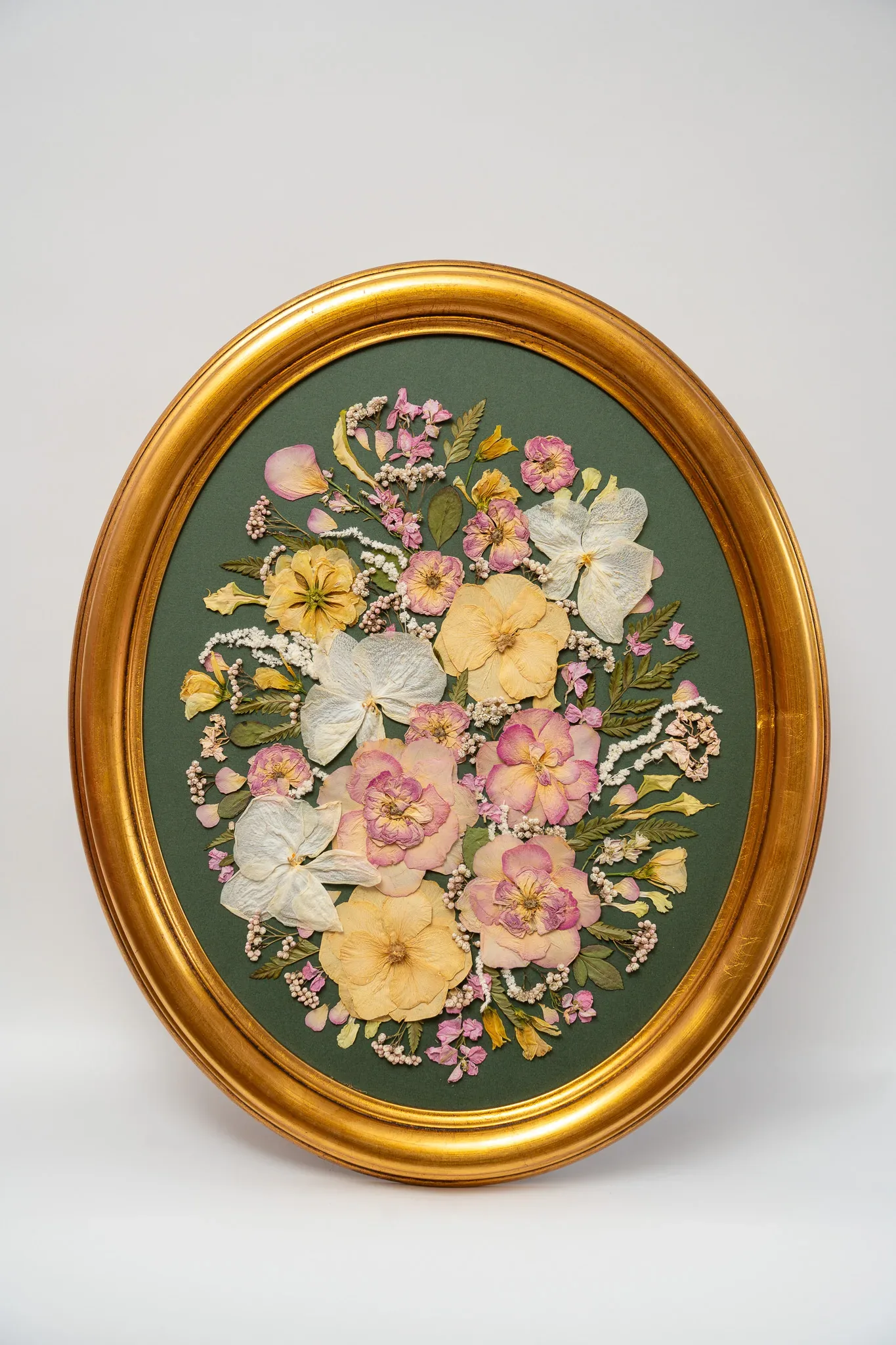 A gold oval frame of pressed flowers on a green mount