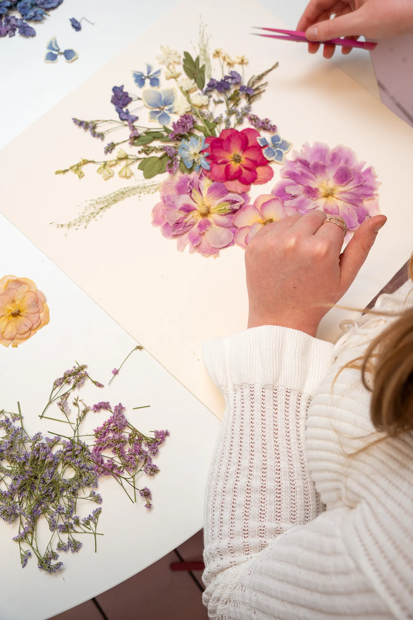 Hands arranging pressed pink flowers with tweezers