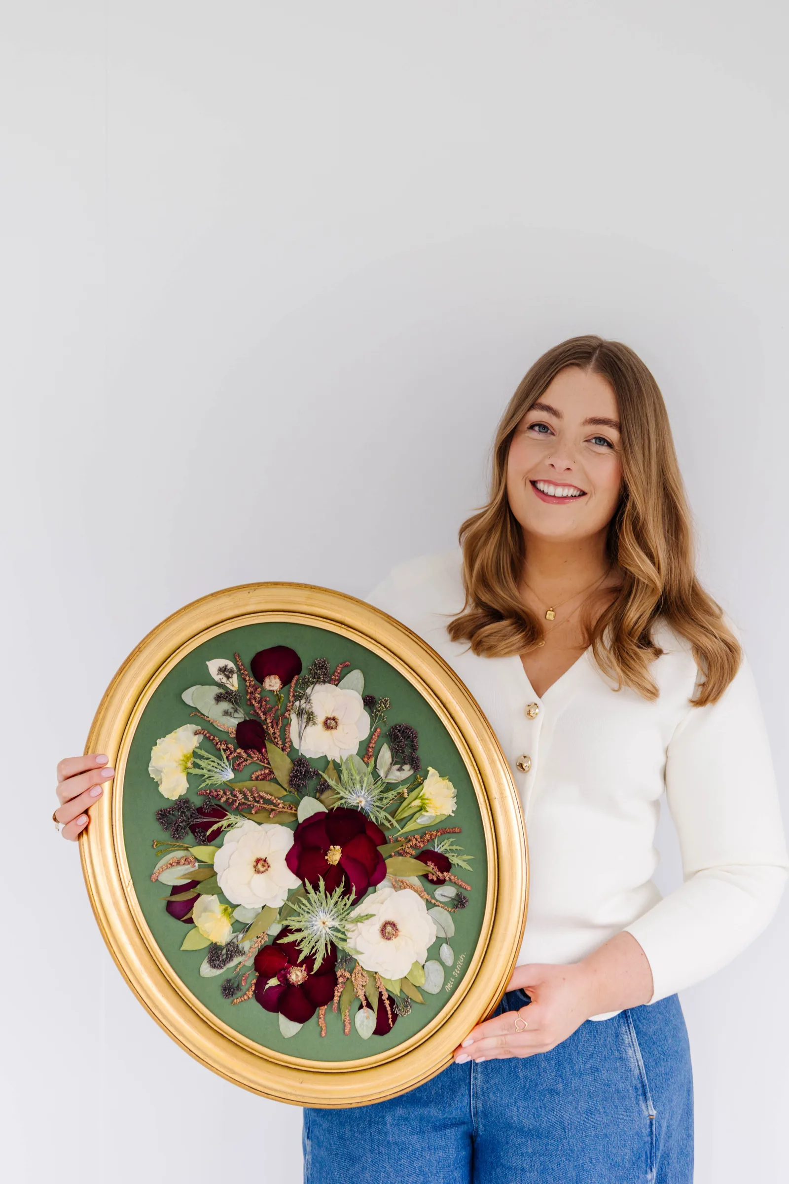 Nell holding a pressed bouquet in a gold oval frame on a green mount