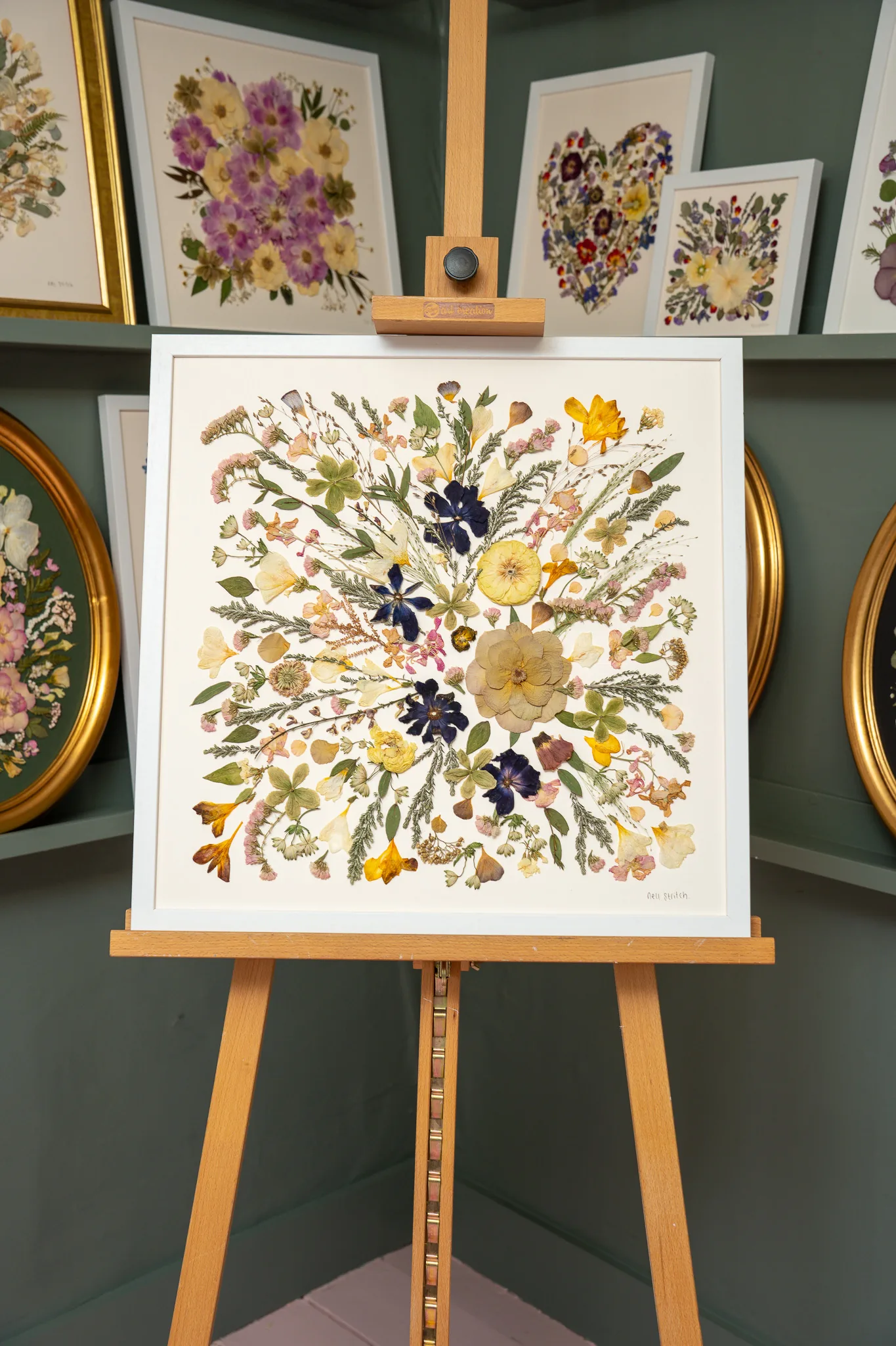 A large square pressed flower piece on an easel in the studio