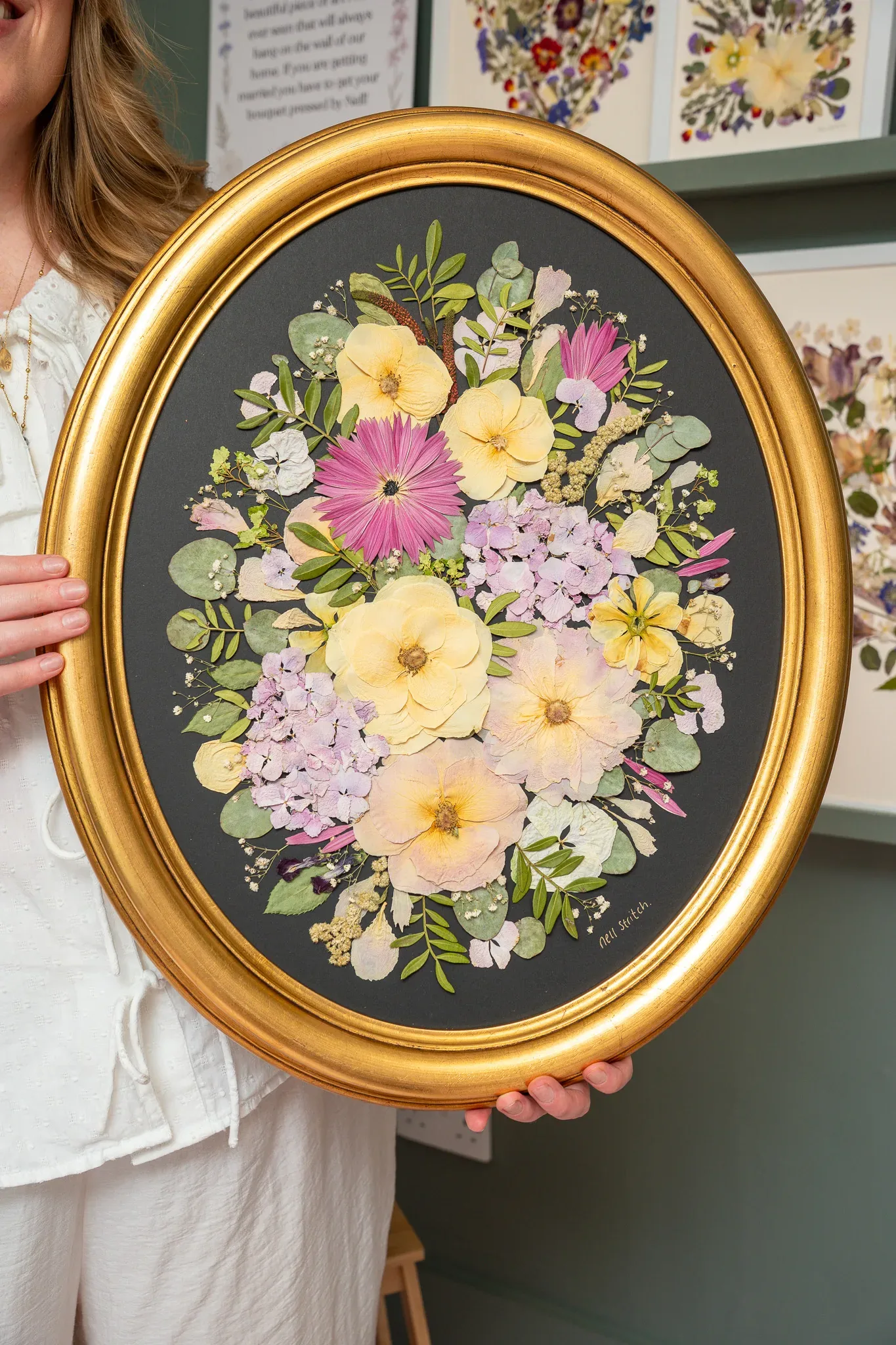Nell holding a pressed bouquet in a gold oval frame on a dark mount