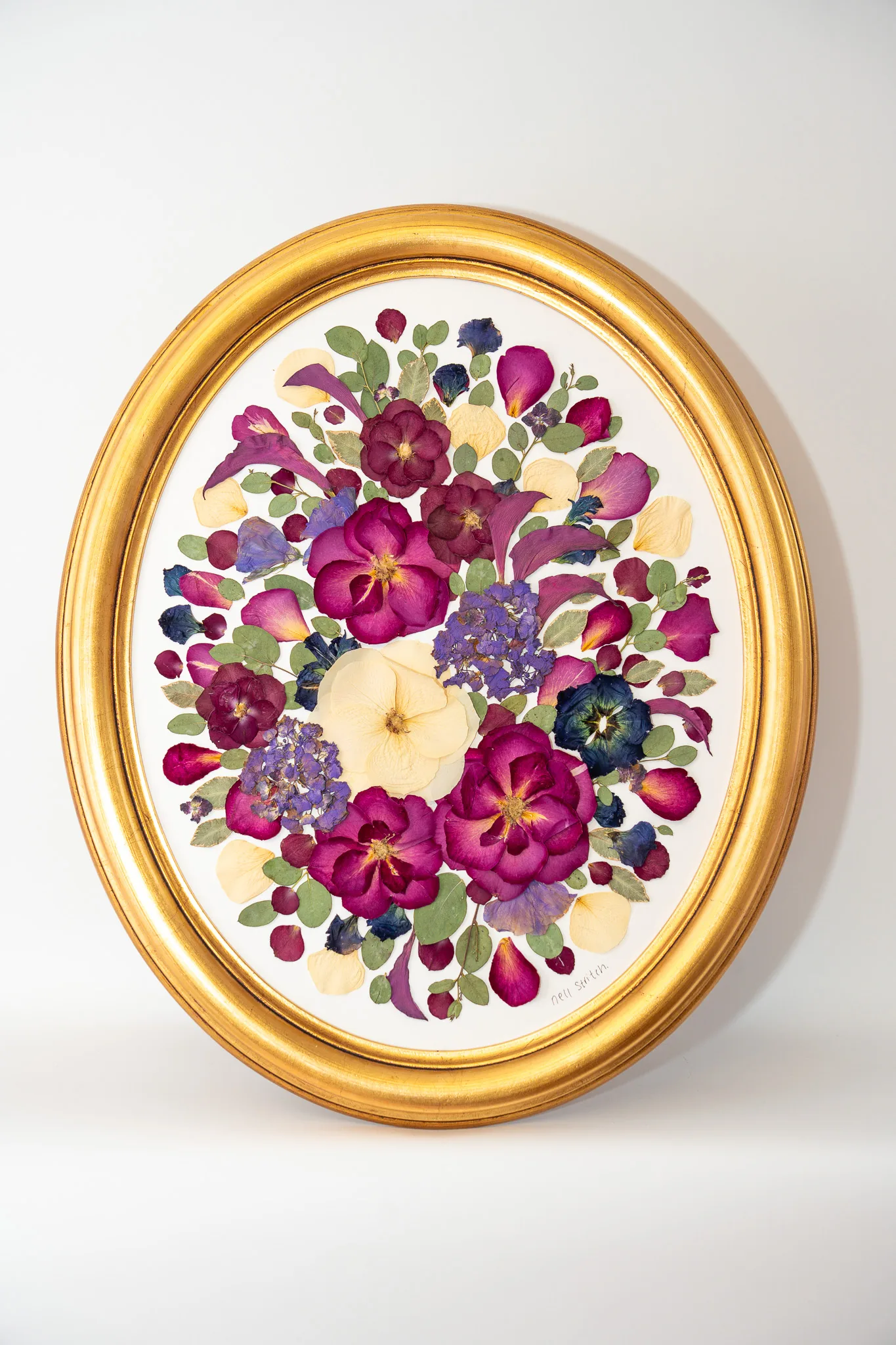 A pressed wedding bouquet in a gold oval frame