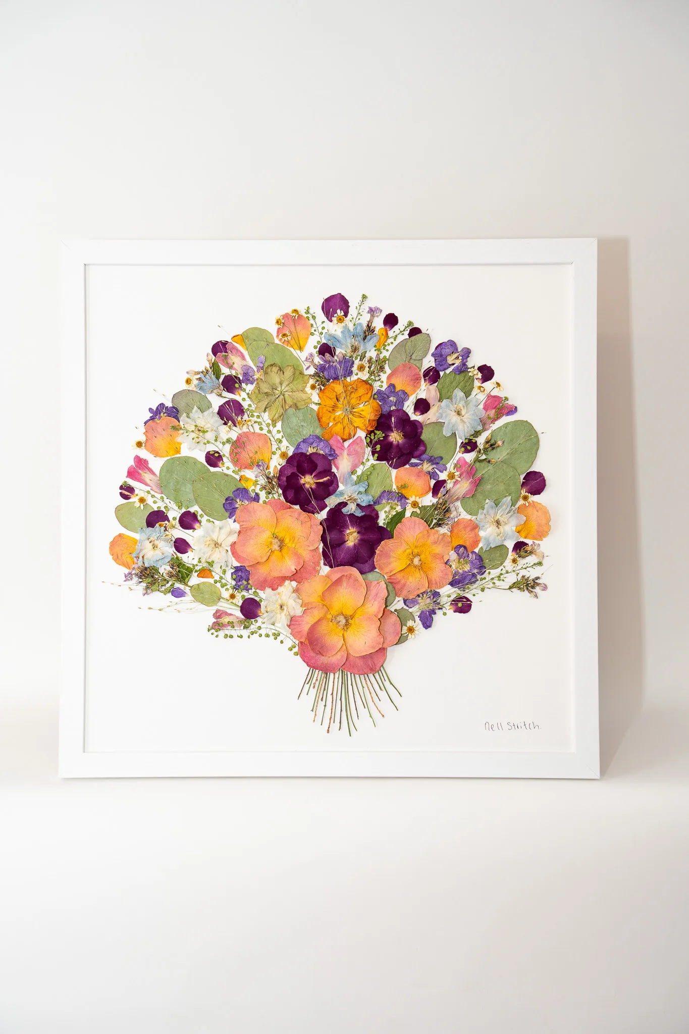 A pressed wedding bouquet in a white square frame