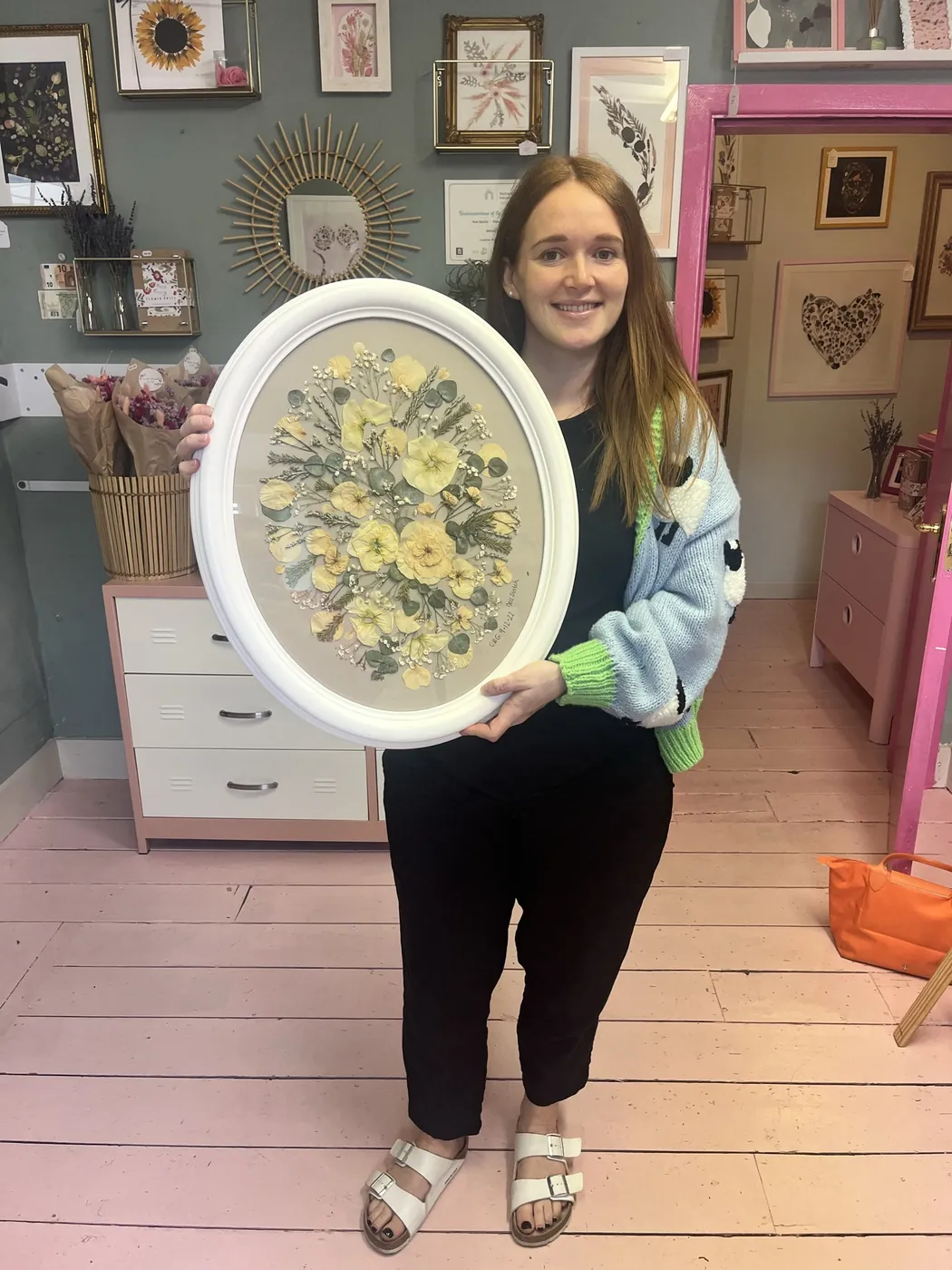 A happy customer holding her pressed flowers in a white oval frame