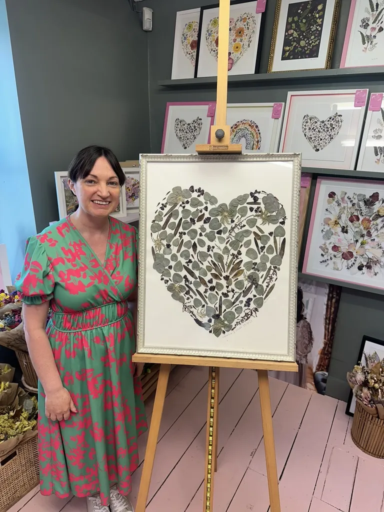 Two friends beside a pressed flower heart in a white frame