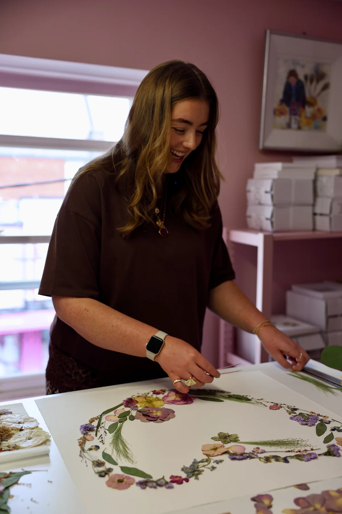 Nell smiling as she arranges pressed flowers into a heart on the studio table
