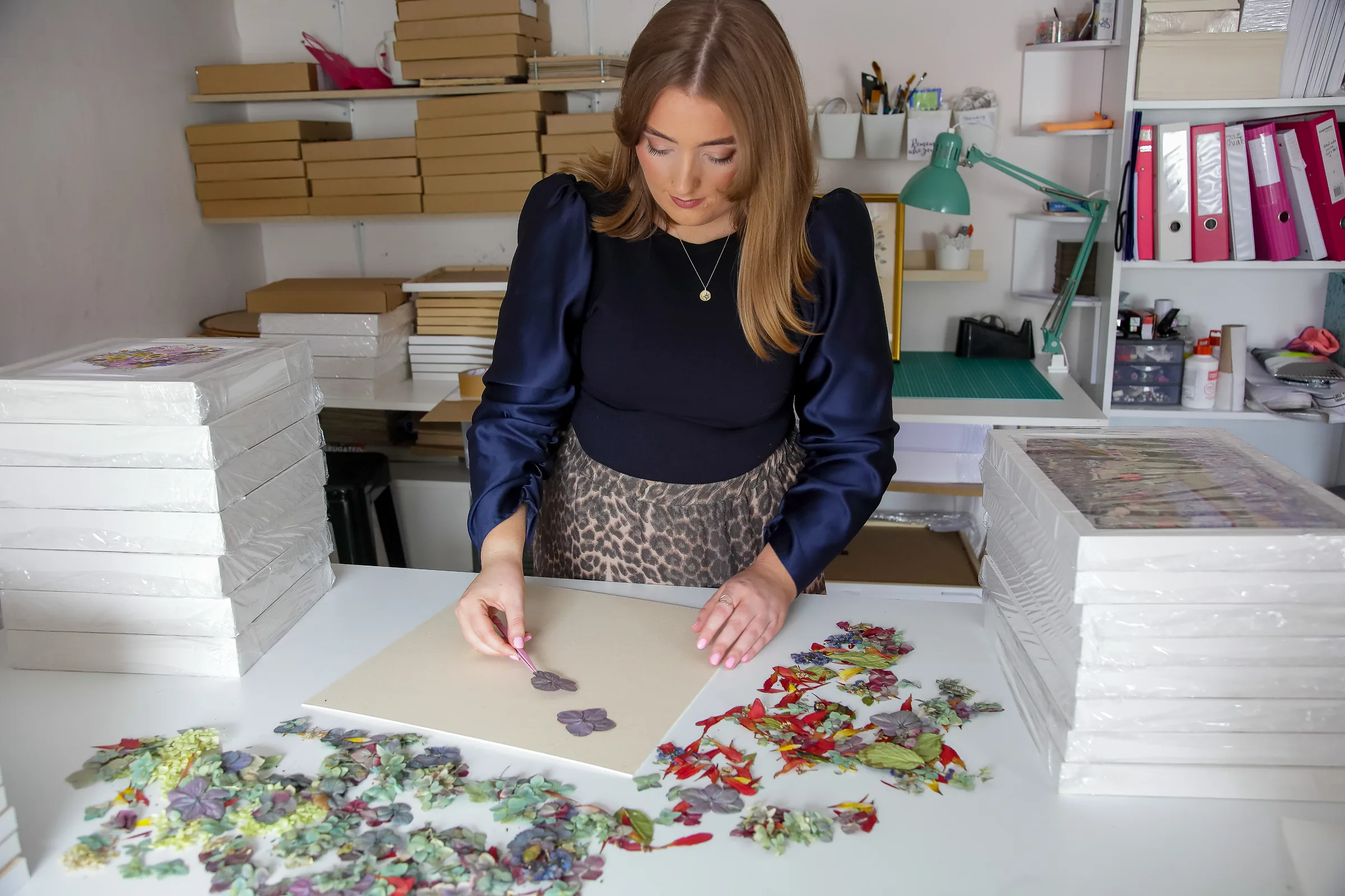 Nell at her studio table, with boxes of frames stacked behind her