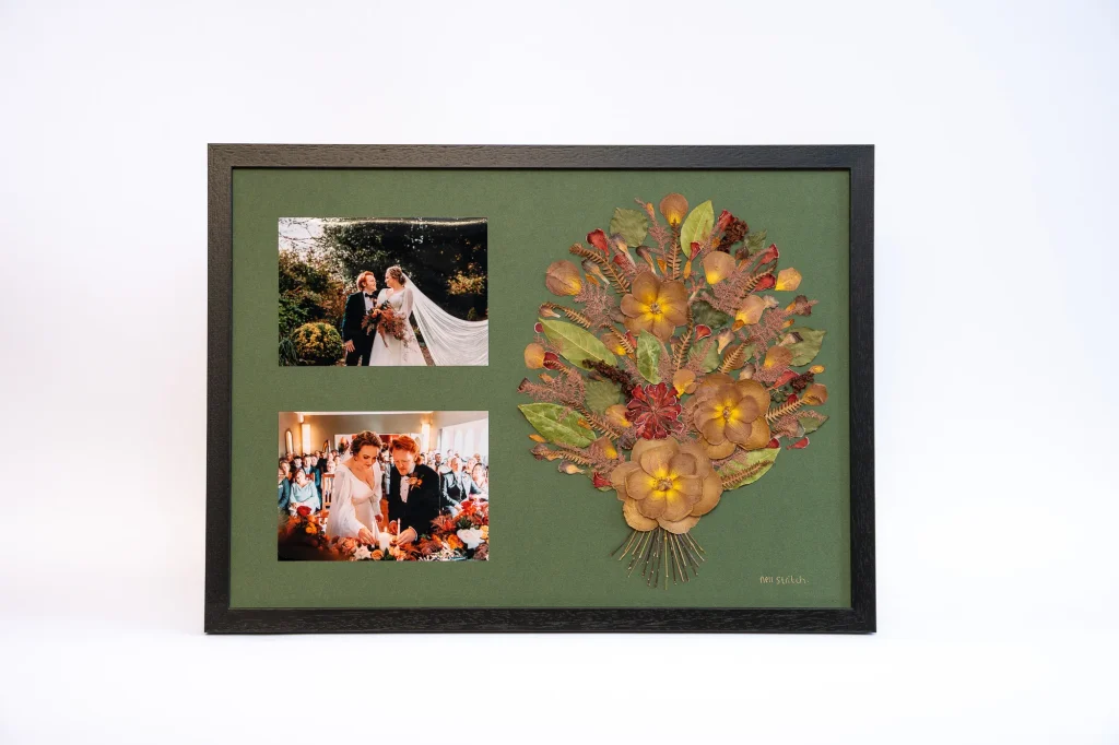 A pressed bouquet on a green mountboard with two photographs beside it, in a black frame