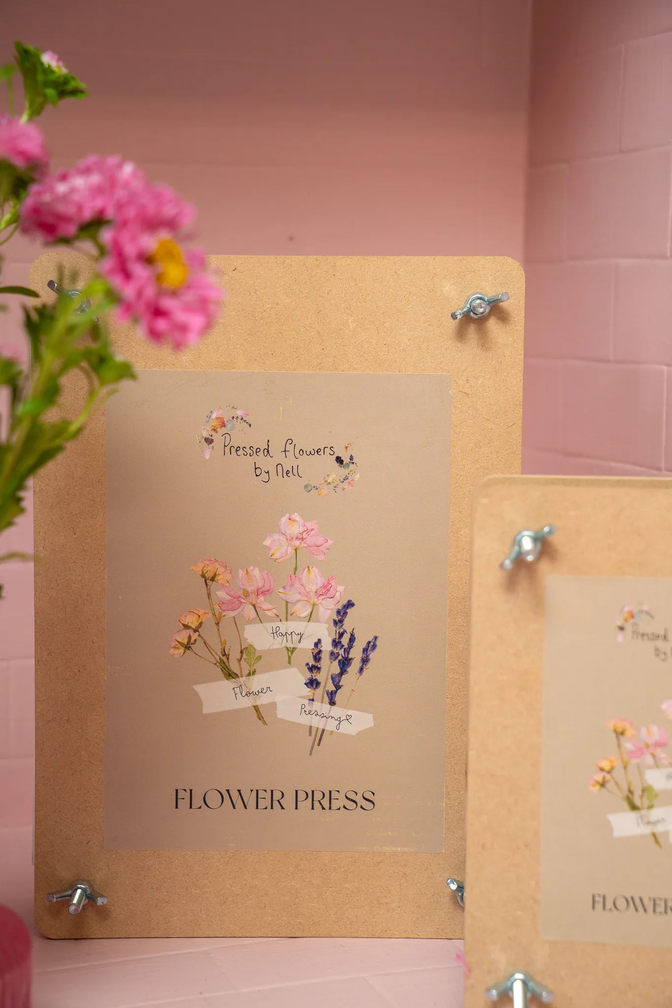 A flower press with a pressed bouquet design beside fresh pink flowers