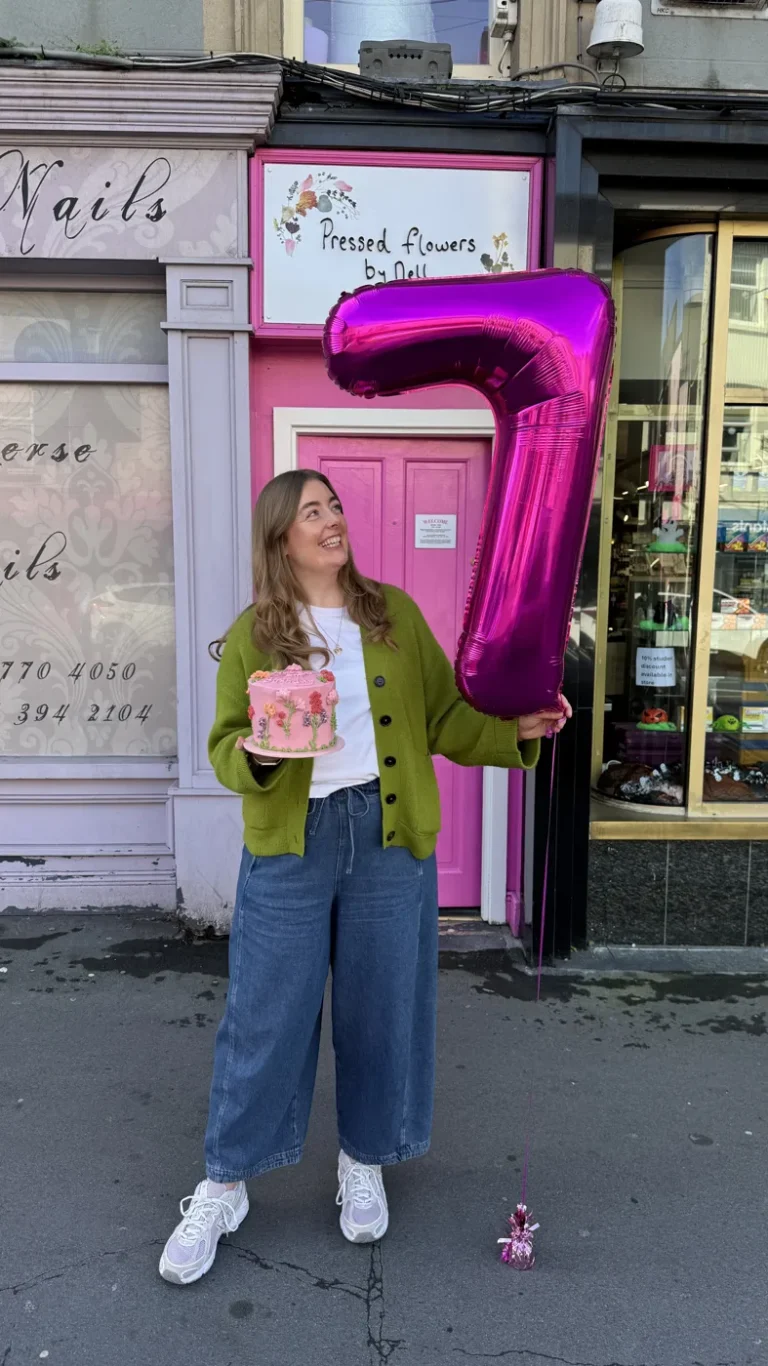 Nell outside the pink studio door with a number seven balloon and a birthday cake