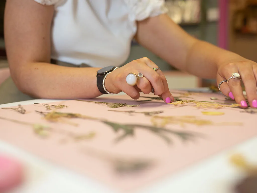 Hands laying pressed flowers on a design at the pink table