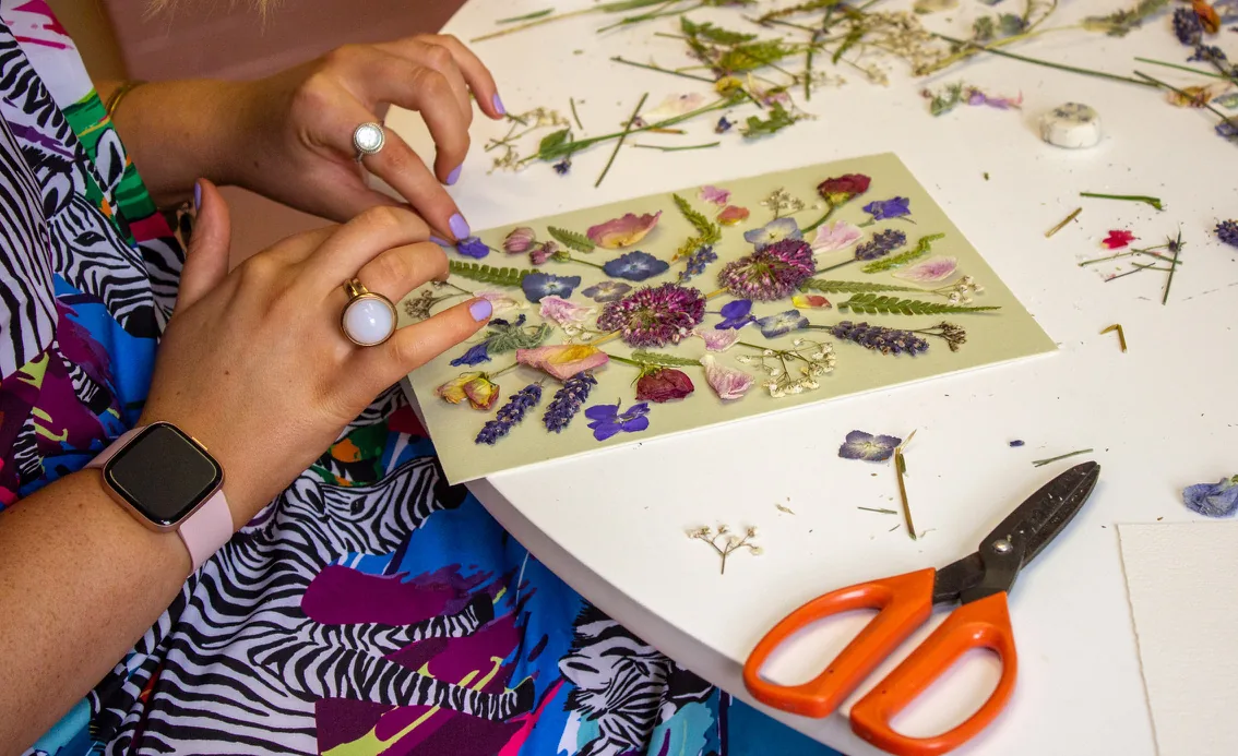 Hands placing pressed flowers with tweezers beside a pair of scissors